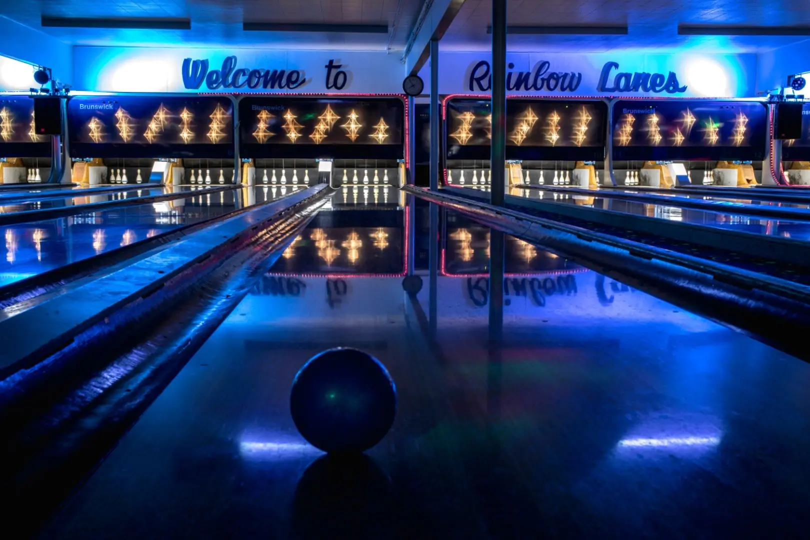 Glow bowling: the lanes lit blue, a ball mid-lane under the Welcome to Rainbow Lanes sign.